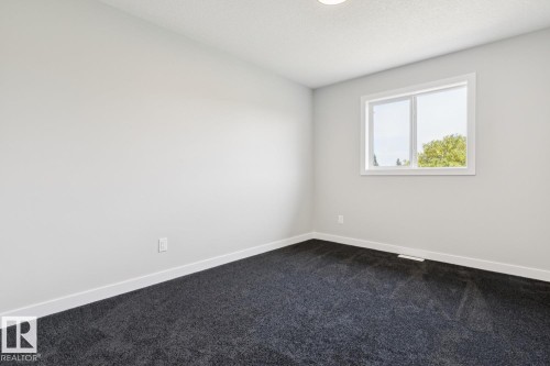 Clean-lined room featuring light gray walls, dark gray carpeting, and a white-framed window - 36 Maple Crescent, Gibbons, AB 