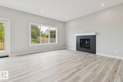 Wood-finish flooring, recessed lighting, and a fireplace with a black herringbone tile surround and white mantel - 36 Maple Crescent, Gibbons, AB 