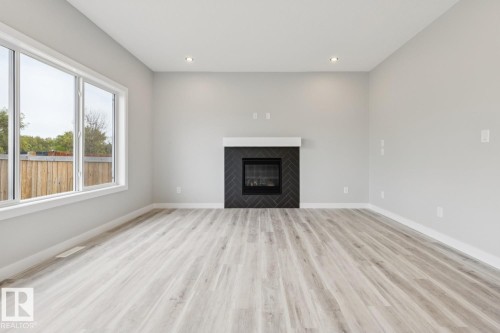 Spacious living area featuring light wood-finish flooring, a contemporary fireplace with a herringbone tile surround, a white mantel, and recessed lighting - 36 Maple Crescent, Gibbons, AB 