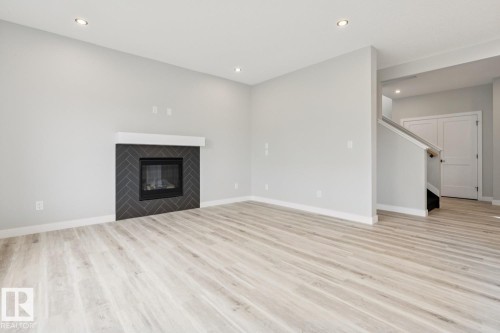 Wood-finish flooring throughout, modern fireplace with a herringbone tile surround, white mantel, recessed lighting, and a staircase with a wooden handrail - 36 Maple Crescent, Gibbons, AB 