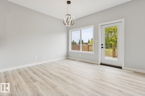 Spacious room with wood-finish flooring, a contemporary pendant light fixture, a large window, and an exterior door with integrated glass - 36 Maple Crescent, Gibbons, AB 