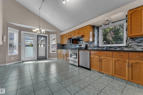Kitchen with wood cabinetry, stainless steel appliances, tile flooring, and a decorative tile backsplash - 9722 157 Street Nw, Edmonton, AB 