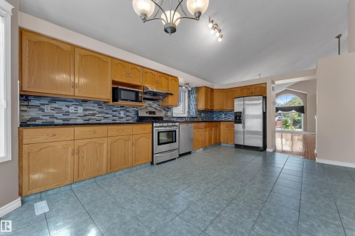 Full kitchen featuring wood-finish cabinetry, stainless steel appliances, blue tile flooring, and a decorative tile backsplash - 9722 157 Street Nw, Edmonton, AB 