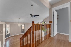 Hardwood flooring throughout, a wood baluster railing, an overhead ceiling fan, a tiered chandelier, and an arched window - 