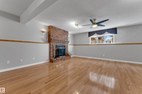 Brick fireplace with a black firebox, wood-finish flooring, ceiling fan, and recessed wall sconces - 9722 157 Street Nw, Edmonton, AB 