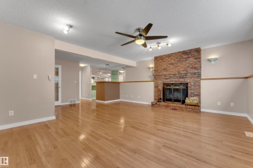 Hardwood flooring, brick-faced fireplace, ceiling fan, track lighting, and a partial wall with a built-in counter - 9722 157 Street Nw, Edmonton, AB 