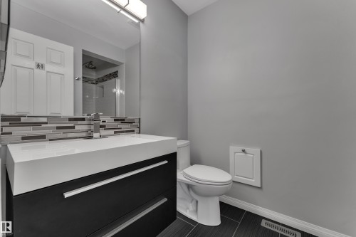 Modern vanity with integrated sink, sleek dark cabinetry, contemporary faucet, mosaic tile backsplash, and large wall-mounted mirror - 9722 157 Street Nw, Edmonton, AB 