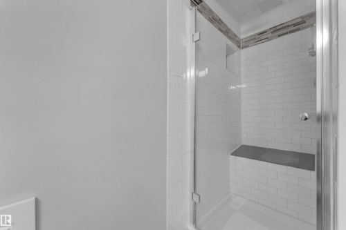 Shower enclosure featuring clear glass panels, subway tile walls, a built-in bench, and an accent tile band - 9722 157 Street Nw, Edmonton, AB 