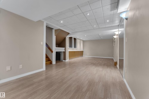 Spacious room featuring wood-finish flooring, recessed lighting, built-in cabinetry, and a carpeted staircase with wood railing - 9722 157 Street Nw, Edmonton, AB 