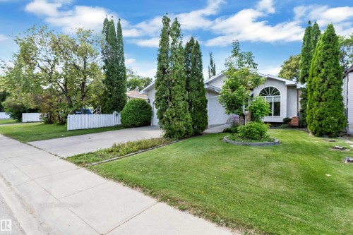 Exterior featuring a curved architectural window, attached garage, concrete driveway, and mature landscaping - 9722 157 Street Nw, Edmonton, AB 