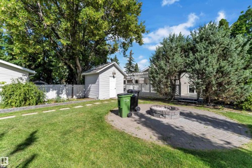 Expansive backyard featuring a paver patio with a built-in fire pit, lush lawn, mature trees, and a detached storage shed - 9722 157 Street Nw, Edmonton, AB 