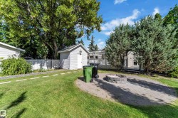 Expansive backyard featuring a paver patio with a built-in fire pit, lush lawn, mature trees, and a detached storage shed - 