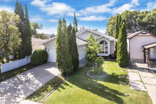 Stucco exterior with an arched window, attached garage, concrete driveway, and front lawn with mature trees and shrubbery - 9722 157 Street Nw, Edmonton, AB 