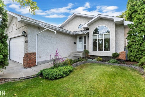 Stucco exterior with brick accents, arched window, attached garage, concrete driveway, and landscaped front yard - 9722 157 Street Nw, Edmonton, AB 