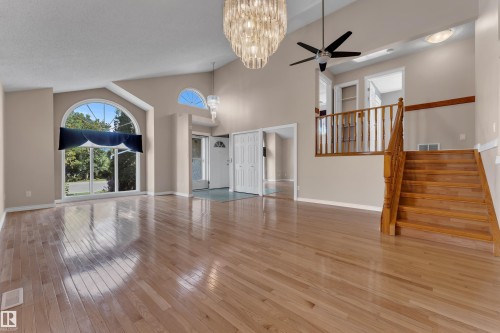 Vaulted ceiling with an ornate chandelier, arched window, wood-finish flooring, and a wooden staircase - 9722 157 Street Nw, Edmonton, AB 