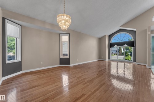 Varnished wood-finish flooring, vaulted ceilings, elegant chandelier, and a large arched window with sliding glass doors - 9722 157 Street Nw, Edmonton, AB 