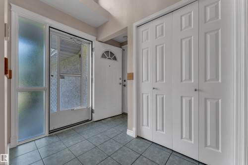 Tiled entryway flooring with a side light panel, a panel door with an arched transom, and bi-fold closet doors featuring recessed panels - 9722 157 Street Nw, Edmonton, AB 