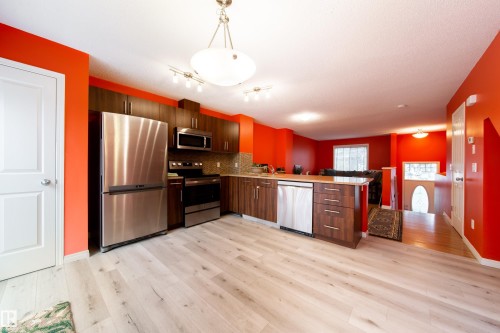 Open-concept kitchen featuring stainless steel appliances, wood-finish cabinetry, a tiled backsplash, and light wood-finish flooring - #31 460 Hemingway Rd Nw, Edmonton, AB 