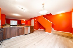 Open-concept living space with light wood-finish flooring, a kitchen island with dark wood-finish cabinetry, and stainless steel appliances - 