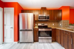 Stainless steel appliances, wood-finish cabinetry, mosaic tile backsplash, composite countertops, and wood-finish flooring - 