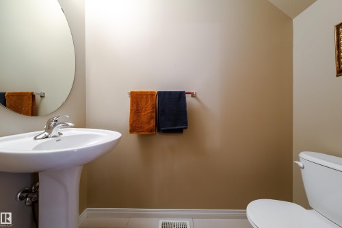 Pedestal sink with chrome faucet, oval mirror, and a white toilet - #31 460 Hemingway Rd Nw, Edmonton, AB 
