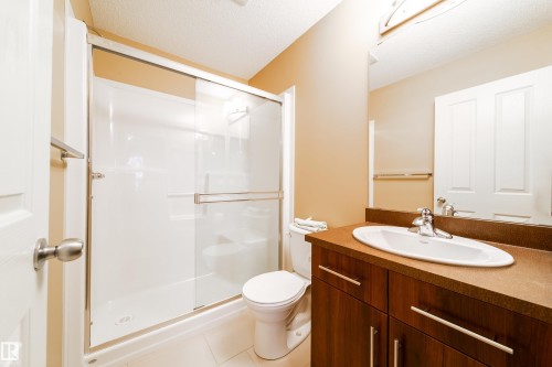 Glass-enclosed shower, wood-finish vanity with an integrated sink, broad mirror, and neutral wall tones - #31 460 Hemingway Rd Nw, Edmonton, AB 