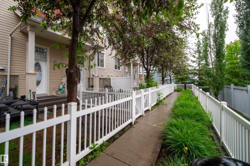 Concrete walkway with a decorative white fence, flanked by vibrant green landscaping - #31 460 Hemingway Rd Nw, Edmonton, AB 