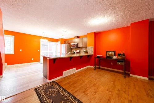 Hardwood flooring, kitchen island with counter seating, stainless steel appliances, wood-finish cabinetry, and glass sliding doors - #31 460 Hemingway Rd Nw, Edmonton, AB 