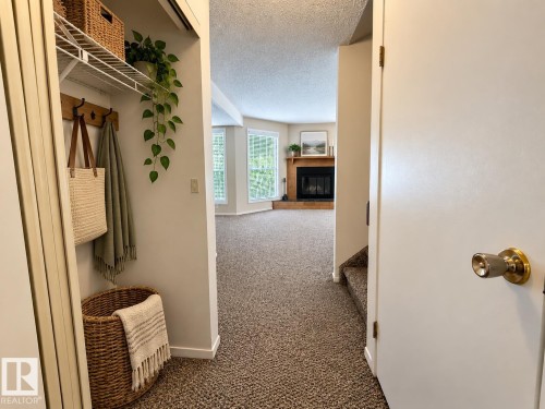 Entryway with built-in coat hooks and shelving, leading to a living area with bay windows and a fireplace featuring a wood mantel - 3526 42 Street Nw, Edmonton, AB 