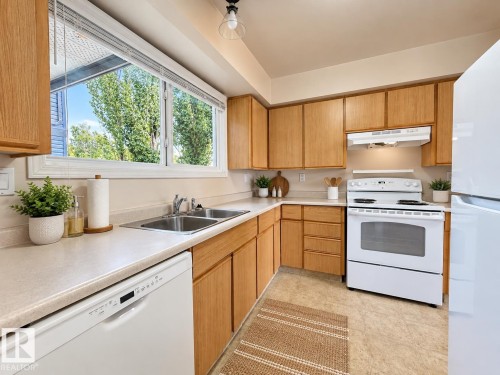 Kitchen featuring wood-finish cabinetry, white appliances, dual basin stainless steel sink, and a large window - 3526 42 Street Nw, Edmonton, AB 