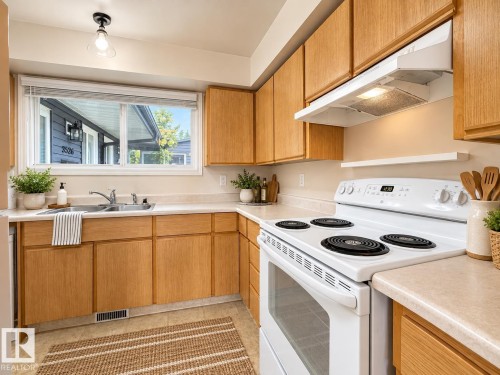Full kitchen featuring a stainless steel double basin sink, white range, wood-finish cabinetry, and neutral countertops - 3526 42 Street Nw, Edmonton, AB 