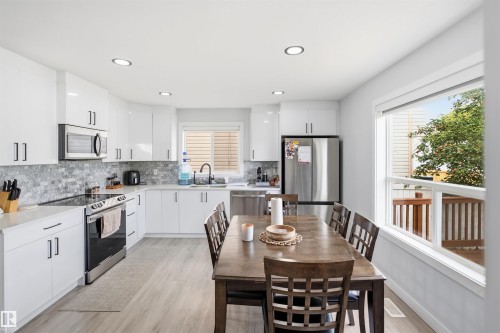 Modern kitchen featuring white cabinetry, stainless steel appliances, mosaic tile backsplash, wood-finish flooring, and recessed lighting - 2122 37 Avenue Nw, Edmonton, AB 