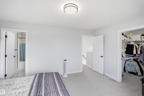 Carpeted room featuring a built-in closet with shelving, a ceiling-mounted light fixture, and a doorway revealing a bathroom with a shower-tub combination - 2122 37 Avenue Nw, Edmonton, AB 