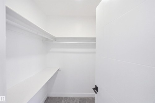 Walk-in closet featuring white built-in shelving, hanging rods, and an interior door with matte black hardware - 2122 37 Avenue Nw, Edmonton, AB 