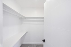 Walk-in closet featuring white built-in shelving, hanging rods, and an interior door with matte black hardware - 