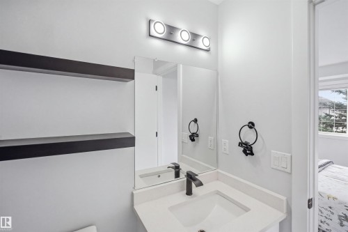 Vanity with a white countertop and integrated sink, matte black faucet, wall-mounted mirror, and overhead vanity lighting - 2122 37 Avenue Nw, Edmonton, AB 