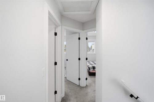 Hallway featuring white walls, white doors with matte black hardware, and gray carpet flooring - 2122 37 Avenue Nw, Edmonton, AB 