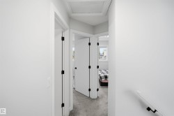 Hallway featuring white walls, white doors with matte black hardware, and gray carpet flooring - 