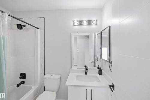 Bathroom featuring a white vanity with an integrated sink, black plumbing fixtures, a wall-mounted medicine cabinet, and a tiled shower surround - 2122 37 Avenue Nw, Edmonton, AB 