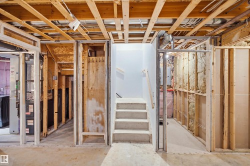 Unfinished basement space with exposed framing, concrete flooring, and an unfinished staircase - 2122 37 Avenue Nw, Edmonton, AB 