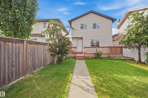 Two-story residence with light-colored siding, a wooden deck with railing, a concrete pathway, a grassy lawn, and a privacy fence - 2122 37 Avenue Nw, Edmonton, AB 