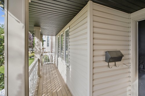 Covered front porch with wood-finish flooring, white railing, and vertical siding - 2122 37 Avenue Nw, Edmonton, AB 