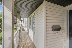 Covered front porch with wood-finish flooring, white railing, and vertical siding - 