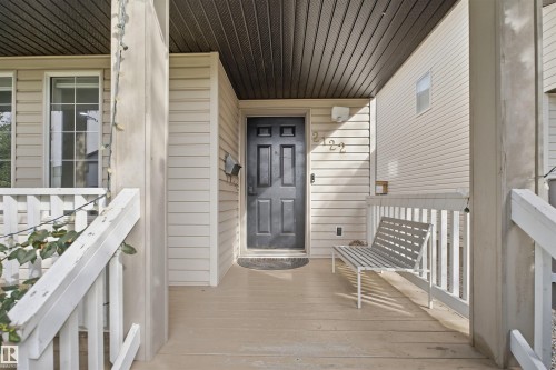 Covered porch with wood-finish flooring, white railing, and exterior wall sconce - 2122 37 Avenue Nw, Edmonton, AB 