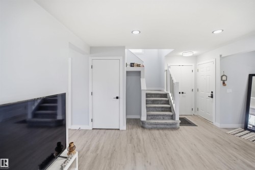 Wood-finish flooring, recessed lighting, white interior doors with black hardware, and a carpeted staircase with white railings - 2122 37 Avenue Nw, Edmonton, AB 