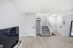 Wood-finish flooring, recessed lighting, white interior doors with black hardware, and a carpeted staircase with white railings - 