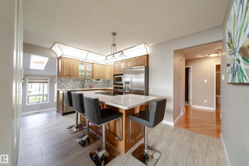 Kitchen featuring light wood cabinetry, stainless steel appliances, a tile backsplash, and an island with a light-toned countertop - 10438 32A Avenue Nw, Edmonton, AB 