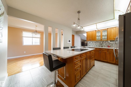Kitchen featuring a central island with cooktop, wood cabinetry, tile backsplash, and stainless steel appliances - 10438 32A Avenue Nw, Edmonton, AB 