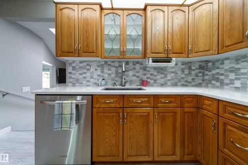Wood cabinetry with arched upper panels, stainless steel dishwasher, mosaic tile backsplash, solid surface countertops, and an undermount sink - 10438 32A Avenue Nw, Edmonton, AB 