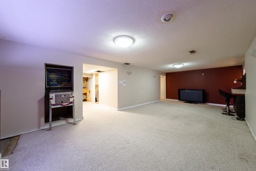 Expansive open room with neutral carpeting, recessed and flush-mount lighting, and a partial accent wall - 10438 32A Avenue Nw, Edmonton, AB 
